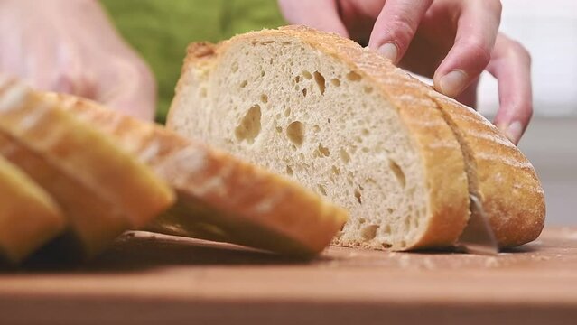 Slicing crusty white bread on cutting board.
