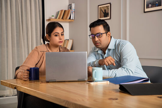 Modern Indian Asian attractive female and male employee busy working together on computer, laptop or woman office worker interacting or talking to senior boss. Business, Finance, cooperation concept.