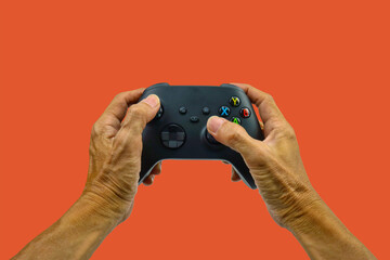Hand of elder man playing video game with joysticks in living room  at home. Entertainment concept..Joystick gaming controller in hand on orange background ,  Entertainment concept.