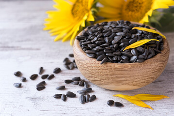 Ripe sunflower seeds in a wooden bowl, sunflowers and petal, scattered seeds on the rustic...