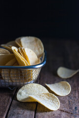 Potato chips in an aluminum basket on a rustic wooden floor.