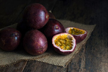 Slice and whole passion fruits put on sackcloth on a rustic wooden floor.