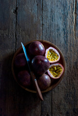 Slice and whole passion fruits with a kitchen knife in a wooden tray on a rustic wooden floor, top view.
