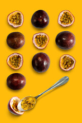 Slice and whole passion fruits with a silver spoon put on a yellow floor, top view.