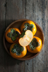 Slice and whole persimmons in a wooden tray on a rustic wooden background.