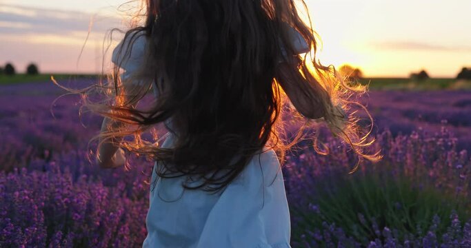 Happy Young Beautiful Woman Running Through Blooming Lavender Field during sunrise
