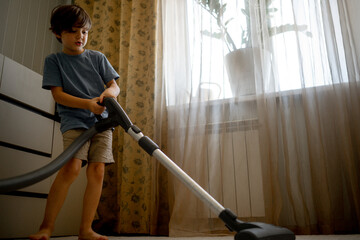 A five-year-old boy helps his parents around the house. The child vacuums the carpet, the boy is taught to clean up the house