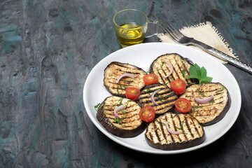 Grilled eggplants in plate on black wood background.