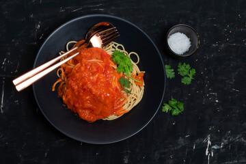 Pasta with tomato sauce in black dish on black wood background