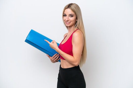 Young sport blonde woman going to yoga classes while holding a mat isolated on white background pointing back