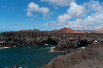 Fototapeta na wymiar Impresionante vista de los acantilados de la costa de las islas canarias de Lanzarote con rocas negras y un hermoso mar. Los hervideros en Lanzarote Islas Canarias con un paisaje volcánico al fondo.
