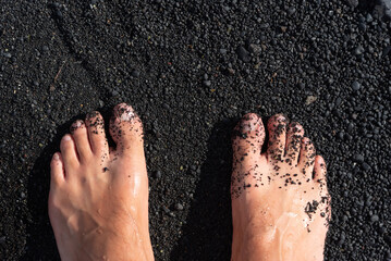 detalle de unos pies caucásicos en una arena negra de una playa de Lanzarote en las Islas canarias.  - obrazy, fototapety, plakaty
