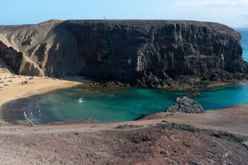 Fototapeta na wymiar vista desde arriba de la playa papagayo en Lanzarote en las islas Canarias. marea baja en la playa con agua trasparente. Turistas tomando el sol en la playa. 