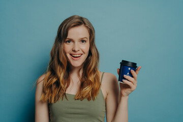 Joyful young girlish woman feeling carefree, holding disposable coffee cup and smiling at camera