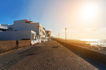 Atardecer en el paseo marítimo de La Santa en Lanzarote. Casas blancas de las isla canarias. sol de frente en la costa.