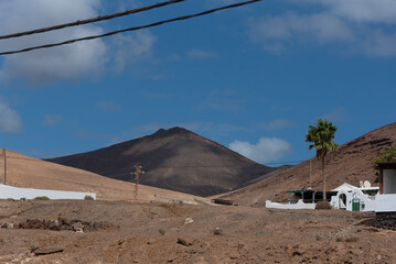 Paisaje volcánico y desértico con palmeras, pequeñas casas blancas y una gran montaña...