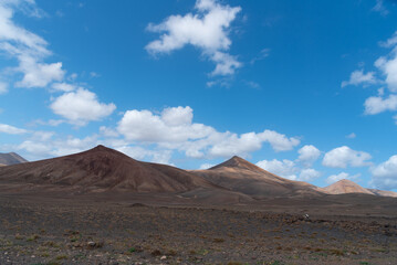 Fototapeta na wymiar Vista panorámica del Parque Nacional de Timanfaya, un paisaje volcánico y desértico con dos grandes montañas en sombra durante un día soleado con el cielo azul y nubes en Lanzarote Islas Canarias.