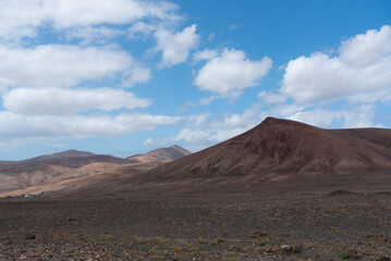 Fototapeta na wymiar Vista panorámica del Parque Nacional de Timanfaya, un paisaje volcánico y desértico con dos grandes montañas en sombra durante un día soleado con el cielo azul despejado en Lanzarote Islas Canarias.