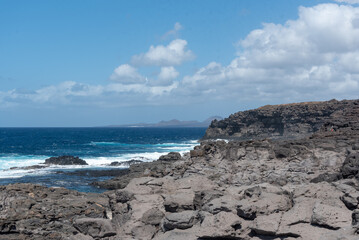 Vista panorámica de la costa de Lanzarote desde un acantilado rocoso, con el mar de color turquesa agitado durante un día soleado con el cielo azul despejado en las Islas Canarias.