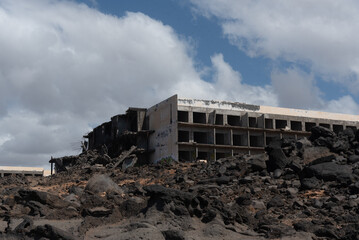 Vista panorámica de un edificio en ruinas y abandonado en un paisaje desértico y rocoso durante un día soleado con el cielo azul y alguna nube en la costa de Lanzarote en Islas Canarias
