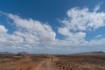 Mujer rubia de espaldas atravesando por un camino un paisaje desértico y volcánico durante un...