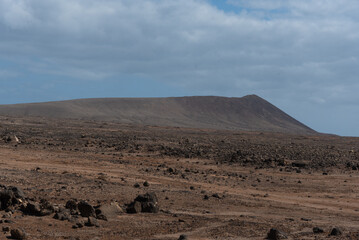 Fototapeta na wymiar Paisaje volcánico y desértico en el parque natural de Timanfaya en Lanzarote, una gran montaña volcánica al fondo durante un día de verano en las Islas Canarias.