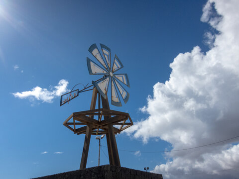 Molino de viento antiguo de madera con las aspas de color azul y blanco con el cielo azul de fondo y alguna nube un d&iacute;a soleado. Energ&iacute;as renovables, energ&iacute;a e&oacute;lica y sostenibilidad.
