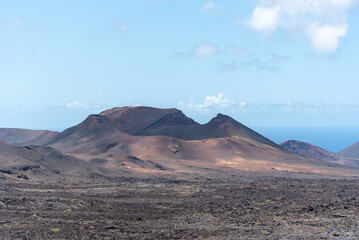 Fototapeta na wymiar Vista panorámica de un paisaje volcánico y desértico con un gran volcán inactivo en medio y el mar al fondo en el Parque Nacional de Timanfaya en Lanzarote. Recursos naturales de las Islas Canarias.