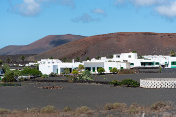 Vista panor&aacute;mica del pueblo Yaiza en mitad de un paisaje volc&aacute;nico con tierra negra y con sus tradicional arquitectura de color blanco y volcanes inactivos al fondo en Lanzarote, Islas Canarias.