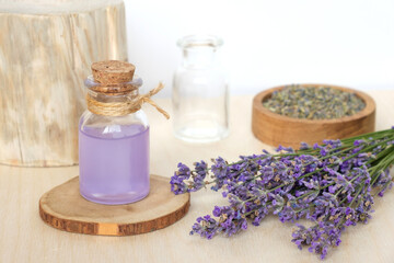 Fototapeta na wymiar Dry lavender flowers in wooden bowl and bottle of essential lavender oil or infused water on white background. Natural organic ingredients for herbal cosmetics. Spa massage set, lavender product
