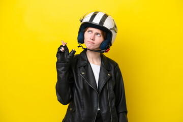 Young English woman with a motorcycle helmet isolated on yellow background with fingers crossing and wishing the best