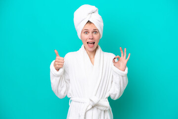 Young woman in a bathrobe isolated on blue background showing ok sign and thumb up gesture