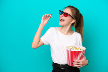 Young English woman isolated on blue background with 3d glasses and holding a big bucket of popcorns