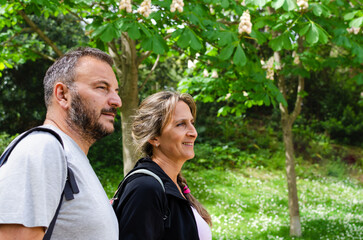 side view of a happy couple walking in the park on a sunny day. they are in their fifties. they have a healthy life carrying their backpacks.