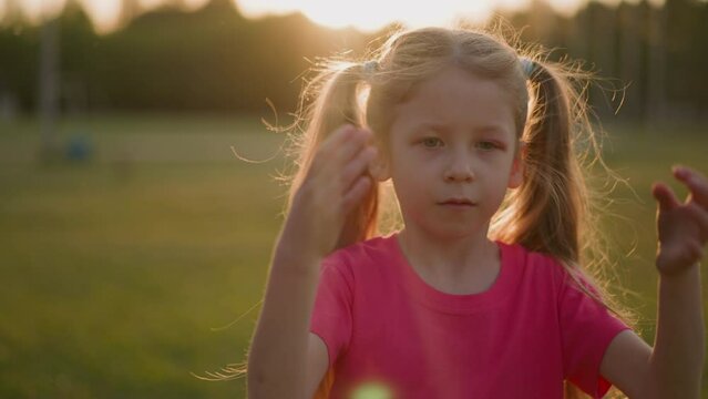 Tired little girl waves to cool down in park at sunset