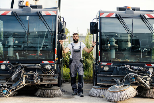 A worker standing next to the street washing vehicles and looking at the camera.