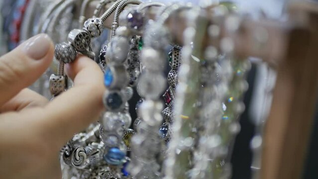 a woman's hand touches and examines silver bracelets in a jewelry store sparkling with the brilliance of precious stones and metal. DOP, close-up, Preference for silver