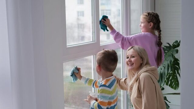 Happy family washes the window. Mom,daughter and son do house cleaning. Mother teaches children to clean windows.
