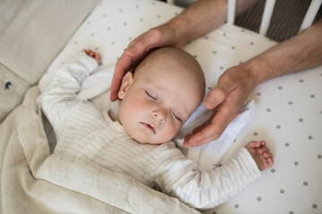Naklejka premium male hands carefully hold the head of a sleeping baby, a small child sleeps in his crib, a child's daytime sleep