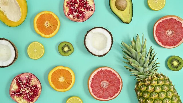 Exotic fruits appear and make summer tropic pattern on cyan background. Stop motion flat lay