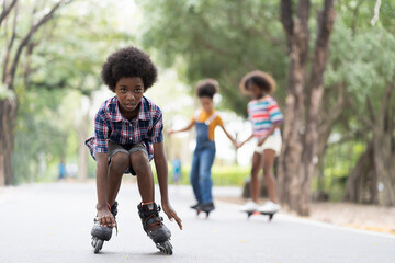 Happy young boy playing on roller blades in the park, African American young boy riding roller...