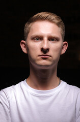 Obraz premium portrait of serious young man with folded and crossing hands standing on dark background. Guy in white t shirt is looking at camera. Confident concept.