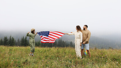 Patriotic holiday in United States of America. Happy family, parents and daughter child girl with American flag in nature on foggy mountains. The USA celebrate 4th of July.