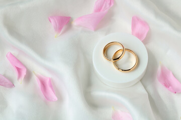 Gold rings on white satin material with pink petals.