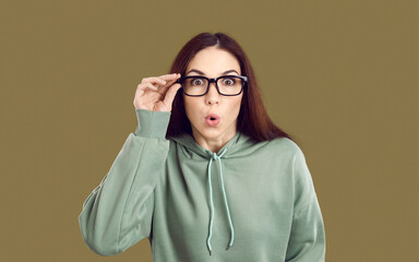 Stunned young Caucasian woman isolated on green studio background take off glasses shocked by...