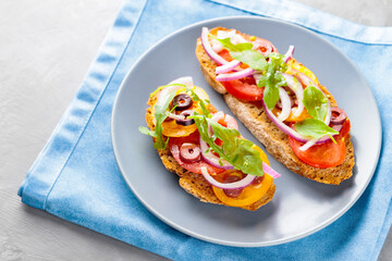 Vegetarian toasts on a gray plate. Bruschetta with tomato, greens and olives. Healthy sandwiches on a blue napkin. Top view