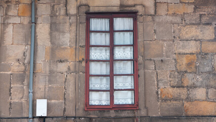 Fototapeta na wymiar Ventana rústica con cortina de encaje en fachada de piedra de palacio