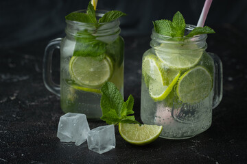 Refreshment mojito cocktail with mint and lime in a glass mug on a black background. Cold summer drink with ice