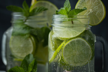 Refreshment mojito cocktail with mint and lime in a glass mug on a black background. Cold summer drink with ice