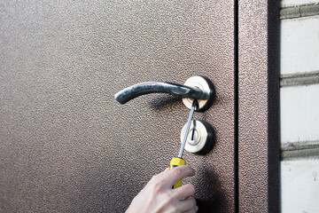 Handyman installing door lock in door with screwdriver. Checking lock for operability in metal door closeup.